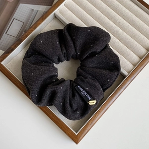 Detail of coffee brown polka dot hair scrunchie with Lucky pendant on velvet display