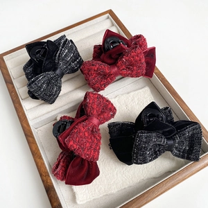 Detail view of tweed bow hair claws in red and grey colors on a wooden jewelry display tray