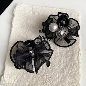 Elegant black lace bow hair clips with pearls and rhinestones on a textured background