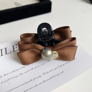 Detail of elegant satin bow hair claw clip with pearl and golden relief coin charm
