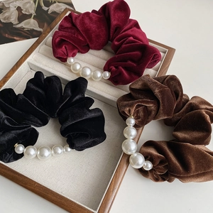 Detailed view of velvet scrunchies in wine red, black and brown with pearl accents