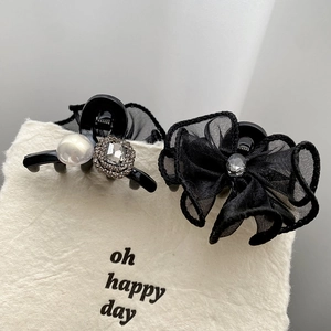 Elegant black bow hair clips with pearls and rhinestones on a minimalist display