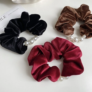 Close-up of velvet hair scrunchies in black, burgundy and brown with pearl details