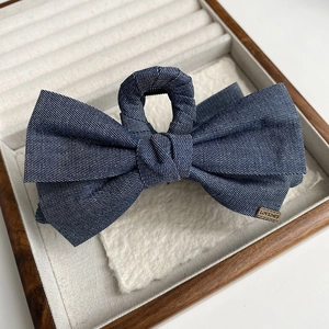 Détail d'une pince à cheveux nœud en denim bleu foncé avec une étiquette dorée gravée