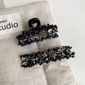 Detail of tweed hair clips with gold flower and black crystals on grey linen fabric
