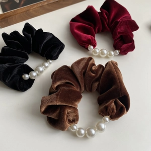 Detail view of velvet hair scrunchies with pearls in black, burgundy and caramel brown