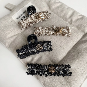 Close-up of tweed hair clips with camellia flowers and pearl charms on a beige linen bag