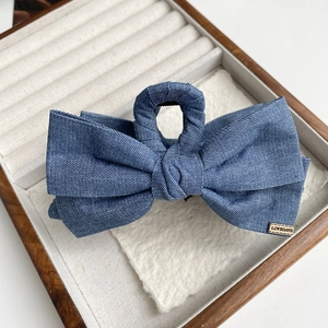 Détail d'une pince à cheveux en denim bleu avec logo doré sur plateau d'exposition