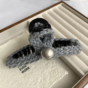 Détail de la pince à cheveux en tricot gris avec perle et ressort métallique robuste
