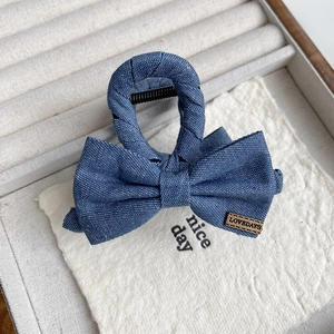 Détail d'une pince à cheveux avec nœud en denim et étiquette sur un plateau blanc