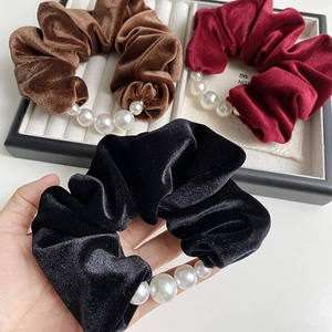 Close-up of velvet hair scrunchies with large pearl details in black, coffee, and burgundy