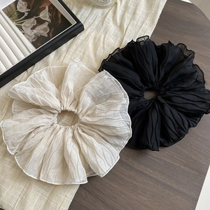 Close-up of pleated oversized hair scrunchies in black and cream on a wooden table