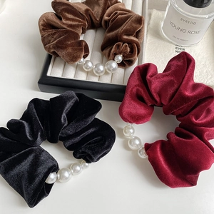 Detailed view of velvet scrunchies with pearls in brown, black, and wine red