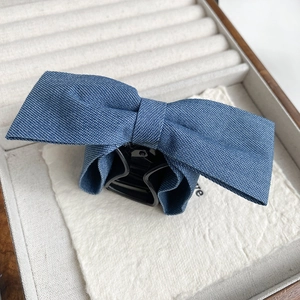 Gros plan d'une pince à cheveux avec nœud en denim bleu sur du papier texturé blanc