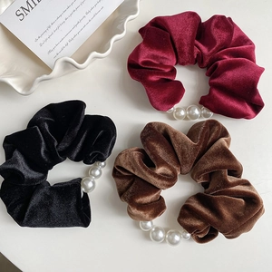 Close-up of velvet scrunchies in wine red, black and brown with pearl embellishments