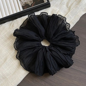 Detail of oversized black ruffled hair scrunchie with textured fabric on a wooden background