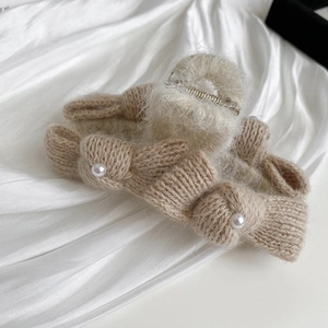 Detail of beige knitted bow hair claw with elegant pearls and white plush fur trim