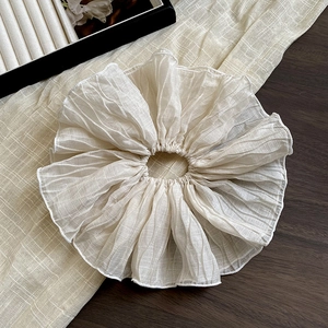 Close-up of pleated cream oversized scrunchie with soft chiffon texture on wood