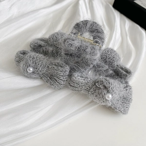 Detail of grey knitted bow hair claw clip with white pearls and gold metal teeth