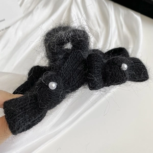 Close-up of black knitted bow hair claw clip with white pearls on a silk background