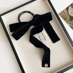Detail of black velvet bow hair scrunchie with long ribbons and gold charms on white frame