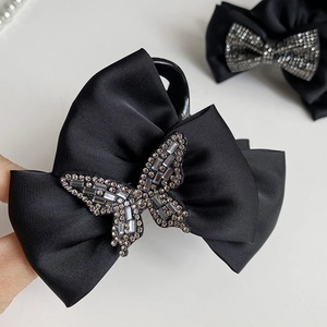 Close-up of a black satin bow hair claw clip featuring a sparkling rhinestone butterfly detail