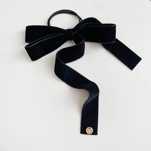 Close-up of black velvet bow hair tie with a decorative gold metal logo pendant