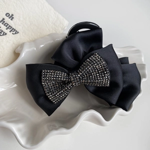 Macro shot of black satin bow hair claw with sparkling rhinestone center on white ceramic