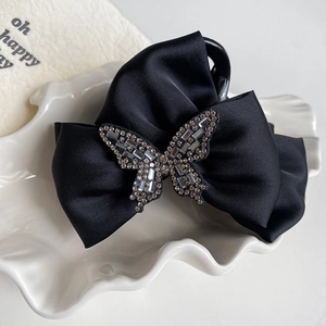 Elegant black satin bow hair claw clip with crystal butterfly detail on white plate