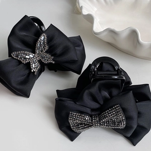 Close-up of black satin bow hair claws with sparkling rhinestones on a white plate
