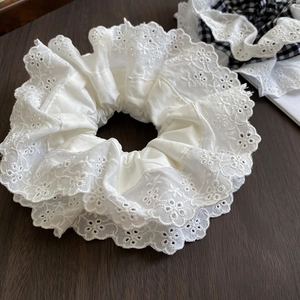 Detail of white lace hair scrunchie with hollow embroidery on a rustic wooden background