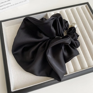 Detailed close-up of a black satin polka dot scrunchie featuring a large pearl ornament