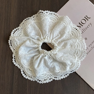 Close-up of a large white lace scrunchie with intricate floral embroidery on wood