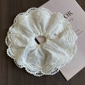 Detailed close-up of large white lace scrunchie with intricate embroidery texture