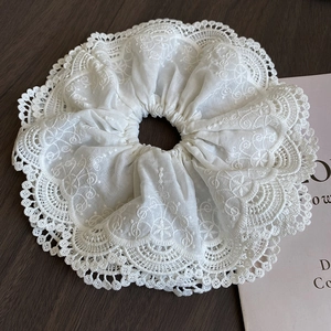 Elegant white lace scrunchie with floral embroidery and ruffle design on a wood surface