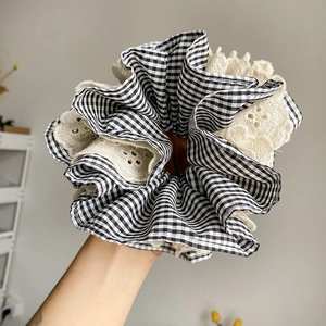 Close-up of oversized gingham and lace scrunchie with detailed hollow-out embroidery