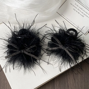 Close-up of black feather hair clips with rhinestone bows on white silk fabric