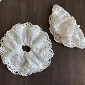 Close-up of white lace scrunchies with intricate floral embroidery and scalloped edges