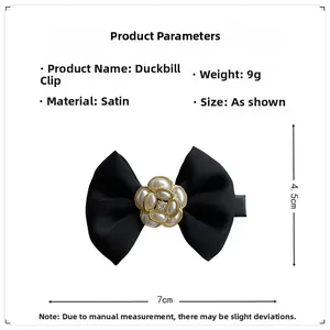 Detail of black satin bow hair clip with white pearl flower and gold metal base