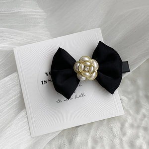 Detailed close-up of a black satin bow hair clip with a pearl camellia and crystal center