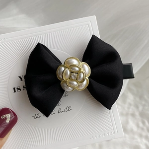 Detailed close-up of a black satin bow hair clip featuring a pearl camellia and golden base