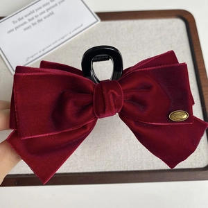 Detail of burgundy velvet bow hair claw clip with golden metal tag and matte black claws