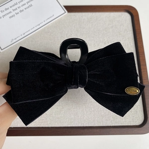 Close-up of velvet bow hair claw clip featuring a gold Wings engraved metal tag