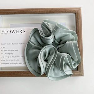Détail d'un chouchou en satin vert clair avec bordure à volants sur fond de bois