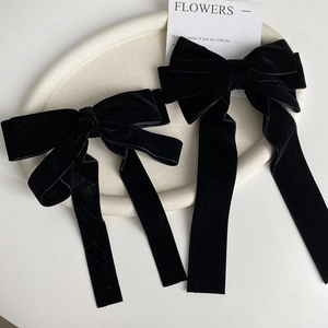 Detail view of two black velvet bow hair clips with long ribbons on a ceramic tray