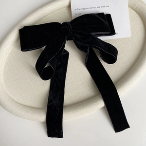 Detail view of a large black velvet bow hair clip with long ribbons on a tray