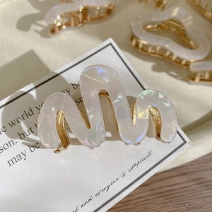 Detailed close-up of S-shaped wave hair claw in pearlescent white with gold metal base