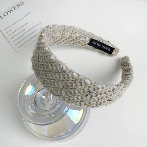 Close-up of beige knitted wide headband with handmade label on glass cylinder
