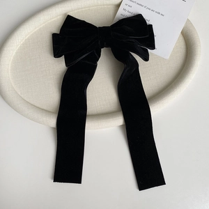 Detail view of a black velvet bow hair clip with long ribbons on a white tray