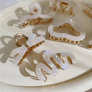 Elegant pearlescent acetate hair claw clips with golden metal base on a beige tray